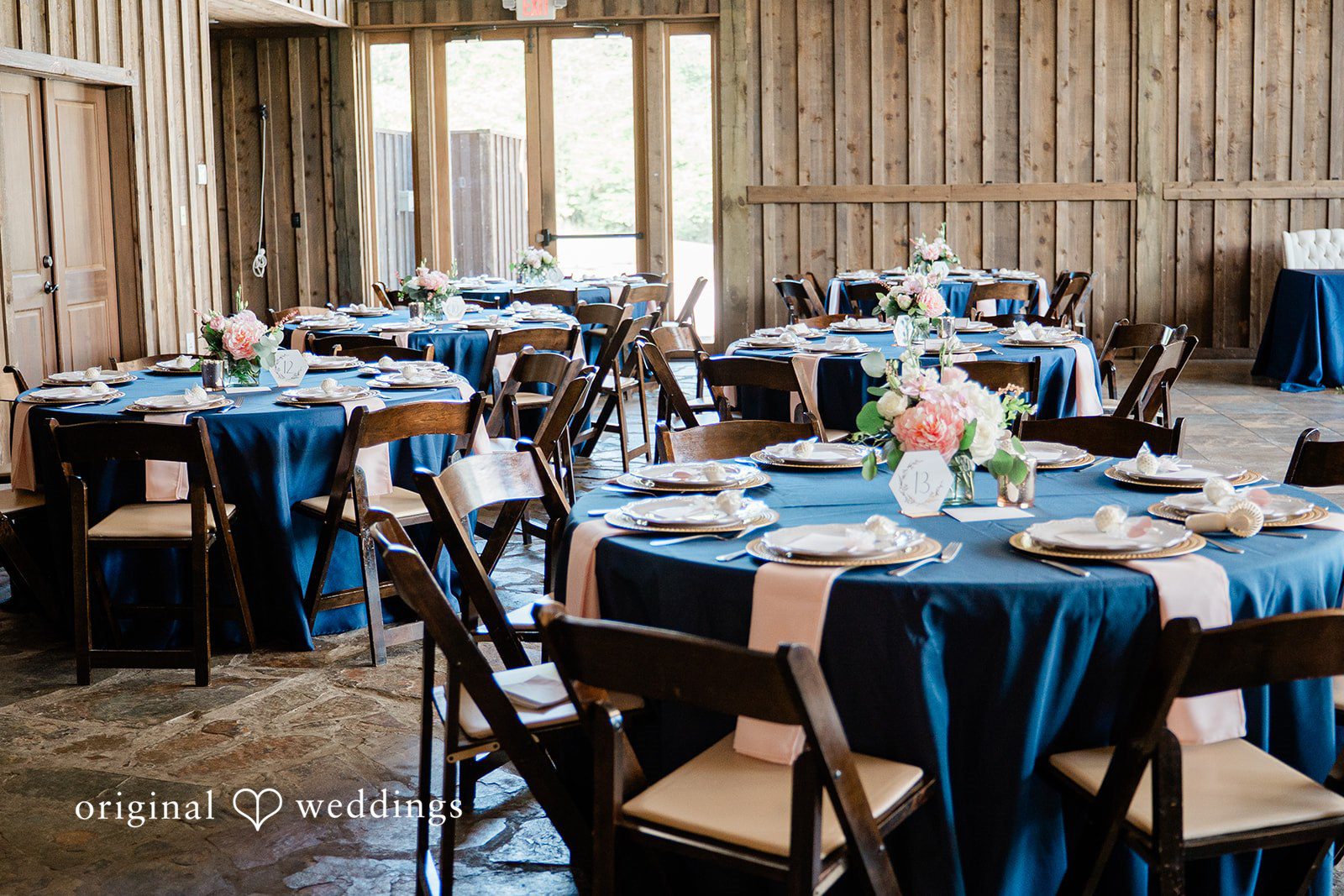 Rustic reception table filled with round and long tables draped in navy blue linens and surrounded by wooden chairs.