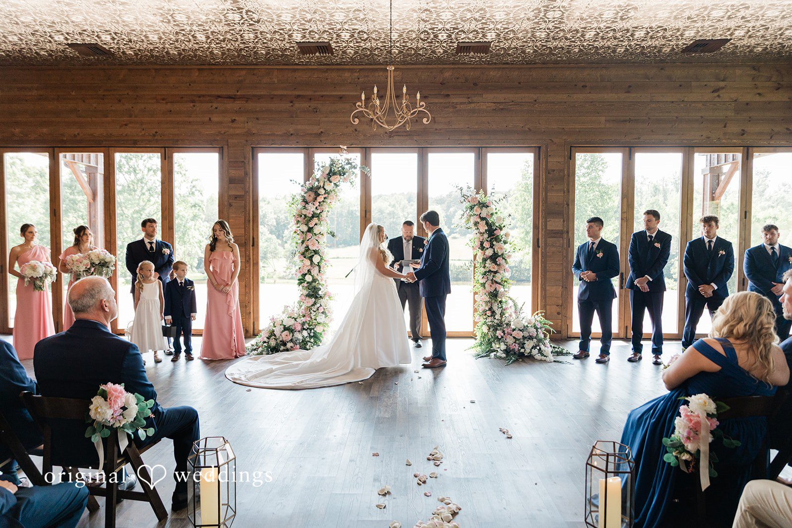 Bride and groom standing together between two tall floral arrangements during their wedding ceremony.