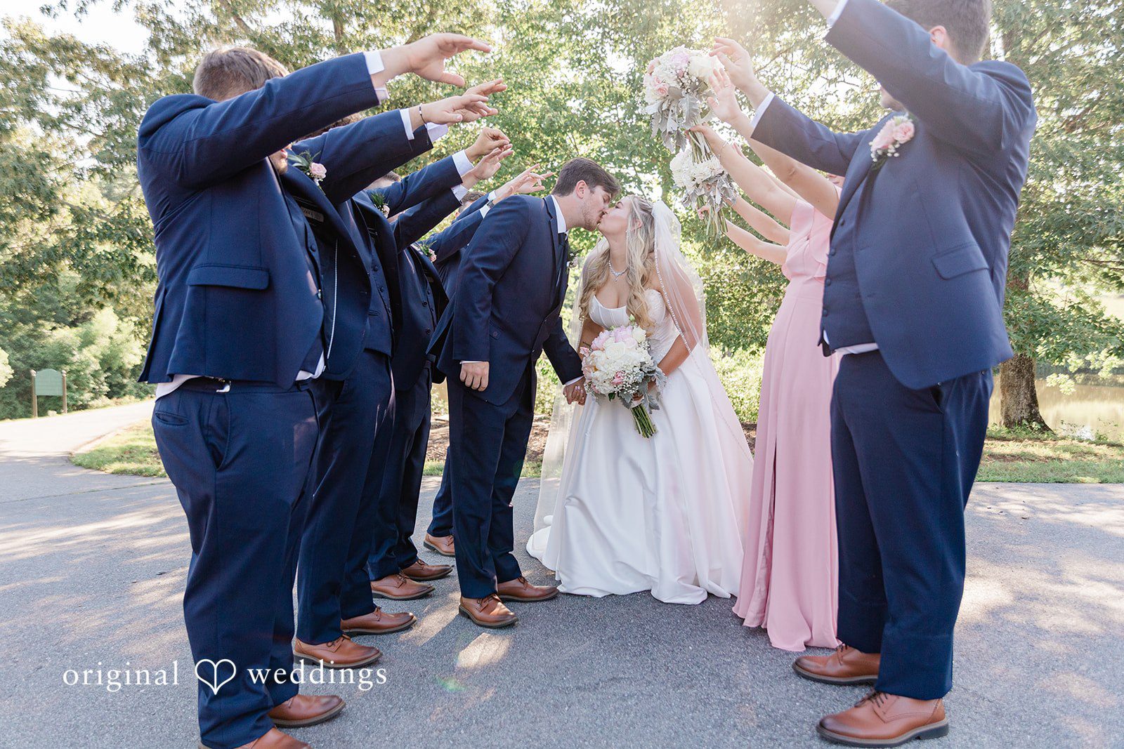 Wedding party cheering and raising their hands around the bride and groom.
