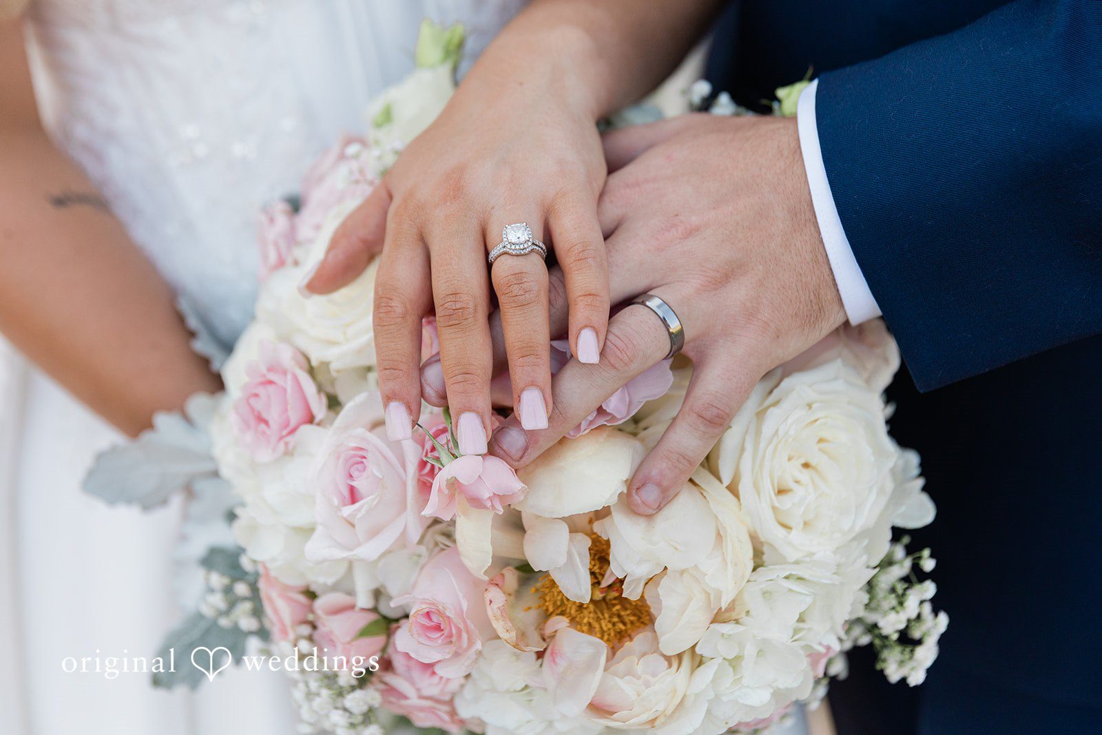 Close-up of a bride and groom's hands showing off their wedding rings over a bouquet of flowers.