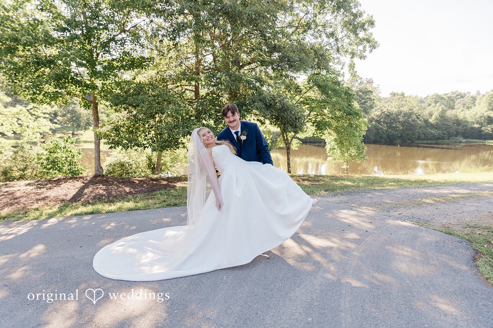 High-angle shot of a groom lifting and swirling his bride in her full white gown on a pathway.