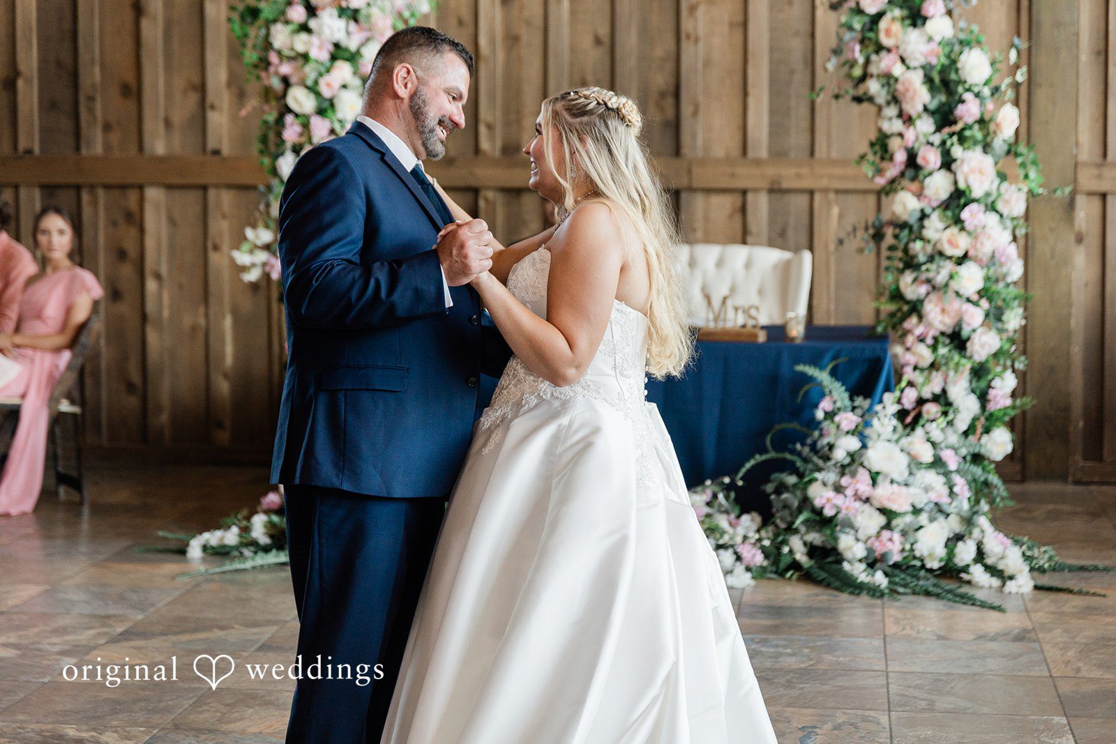 Side profile view of a bride and man dancing together near a floral wedding arch.