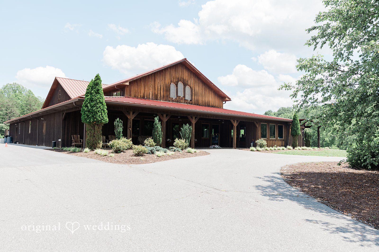 Large wooden barn with a dark roof and a paved driveway leading to the entrance.