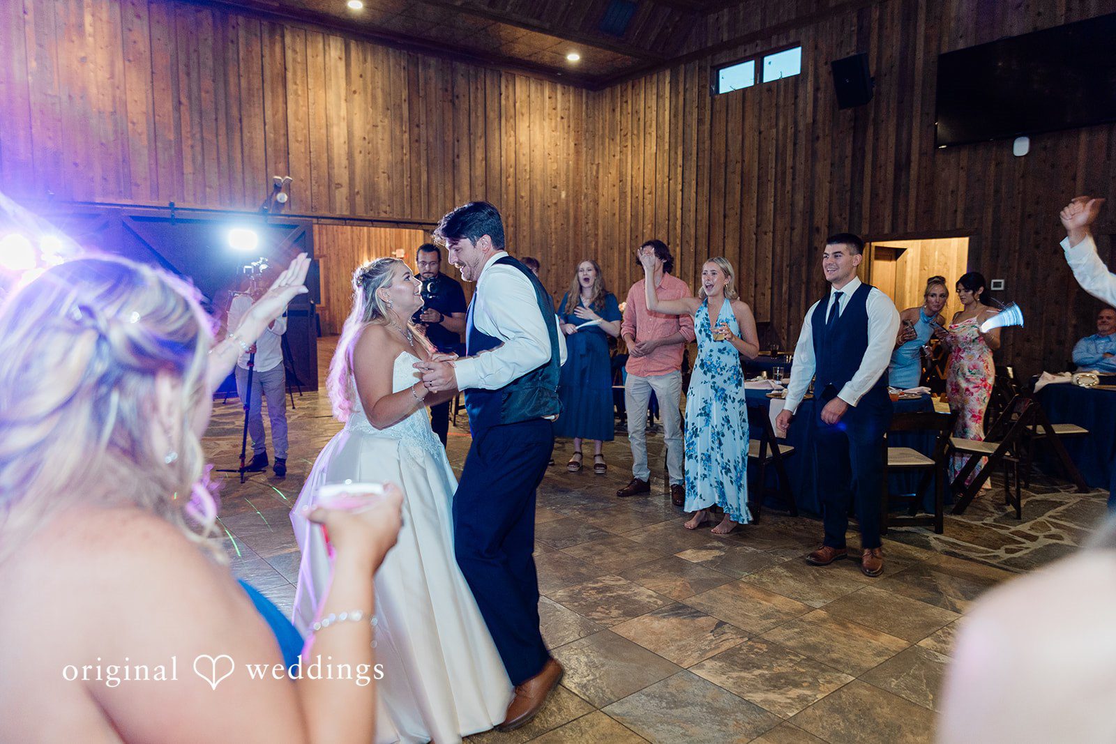 Bride and groom dancing energetically on a crowded dance floor under colorful party lights.