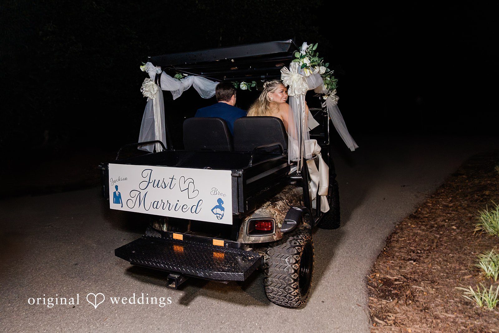A bride and groom driving away in a decorated golf cart with a "Just Married" sign on the back.