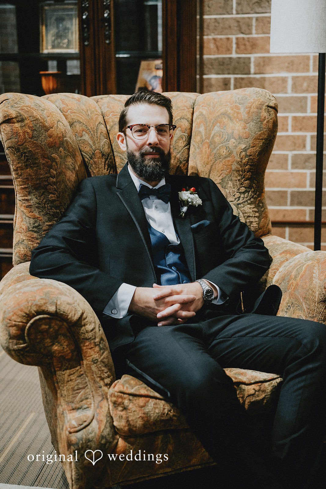 Daniel + Amanda A smiling groom with a beard and glasses sitting in a large armchair.