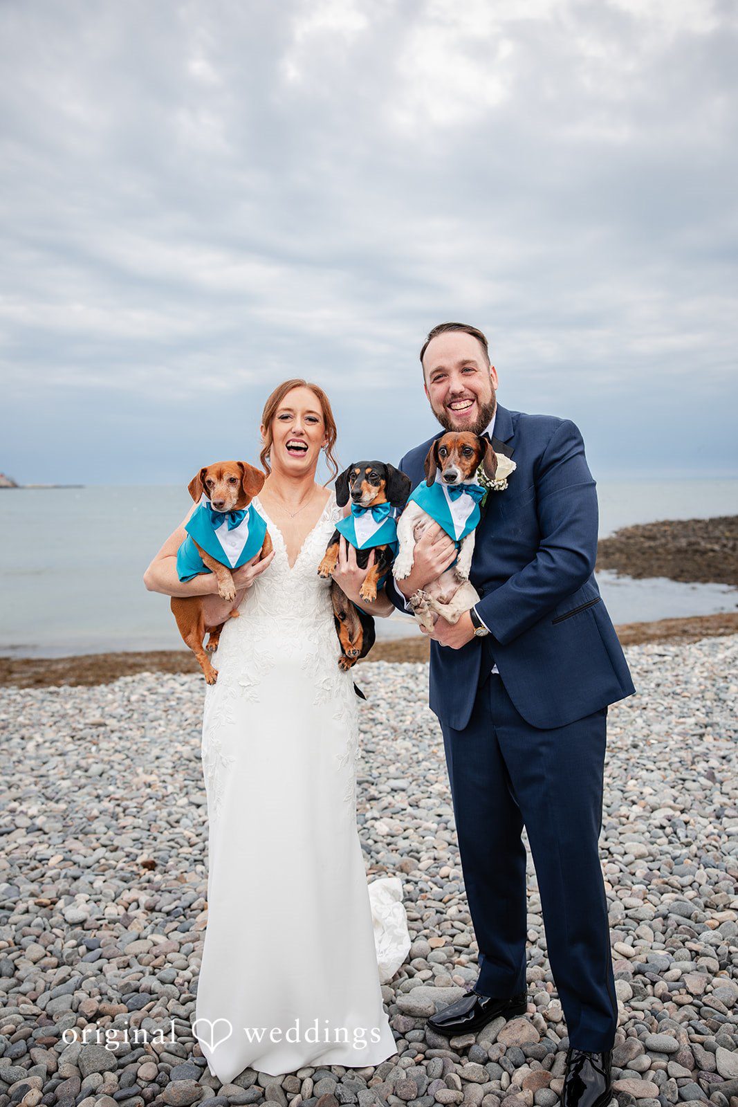 Couple holding their dog together by the ocean after the ceremony