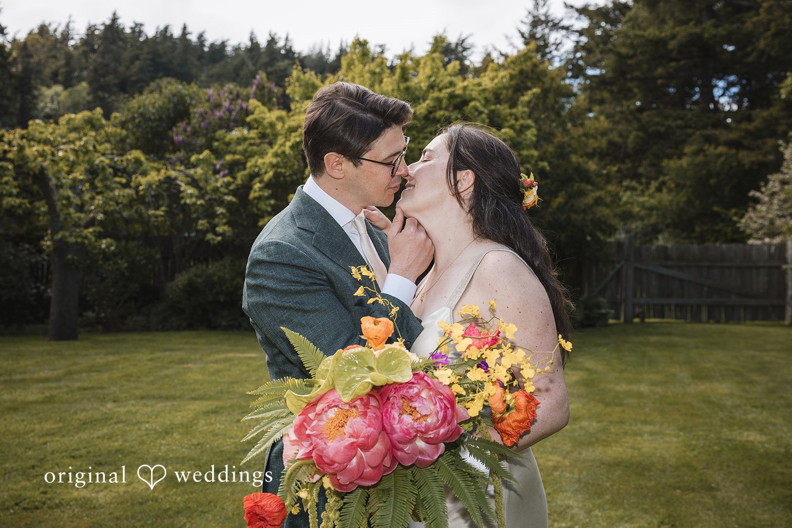 Benjamin + Amber The couple shares a romantic kiss while holding a vibrant bouquet on the lawn after their wedding ceremony