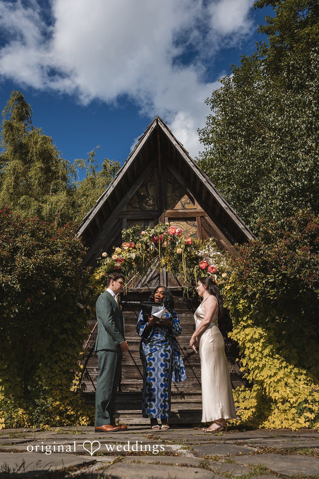 Benjamin + Amber Couple exchanges vows beneath a floral arch during an intimate outdoor wedding ceremony at Outlook Inn captured by Seattle wedding photographers from Original Weddings