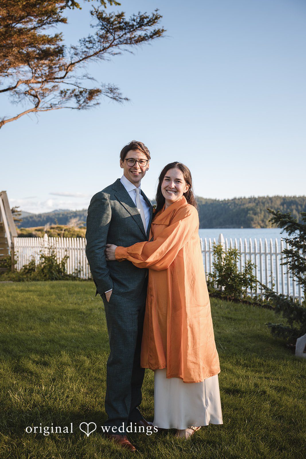 Benjamin + Amber The couple embraces and smiles by the waterfront during golden hour after their wedding celebration