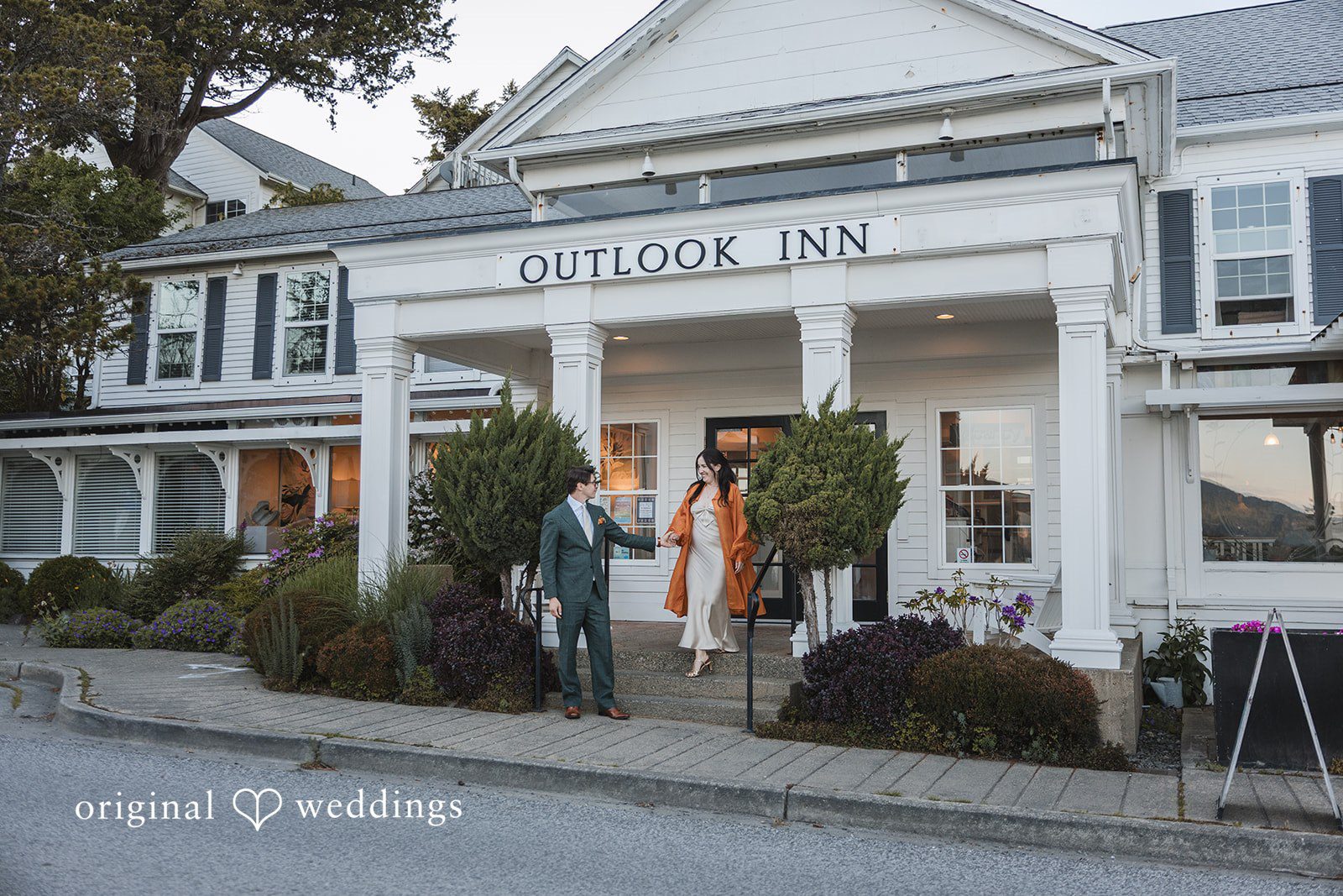 Benjamin + Amber The couple poses joyfully in front of the iconic Outlook Inn entrance after their wedding celebration at Outlook Inn.