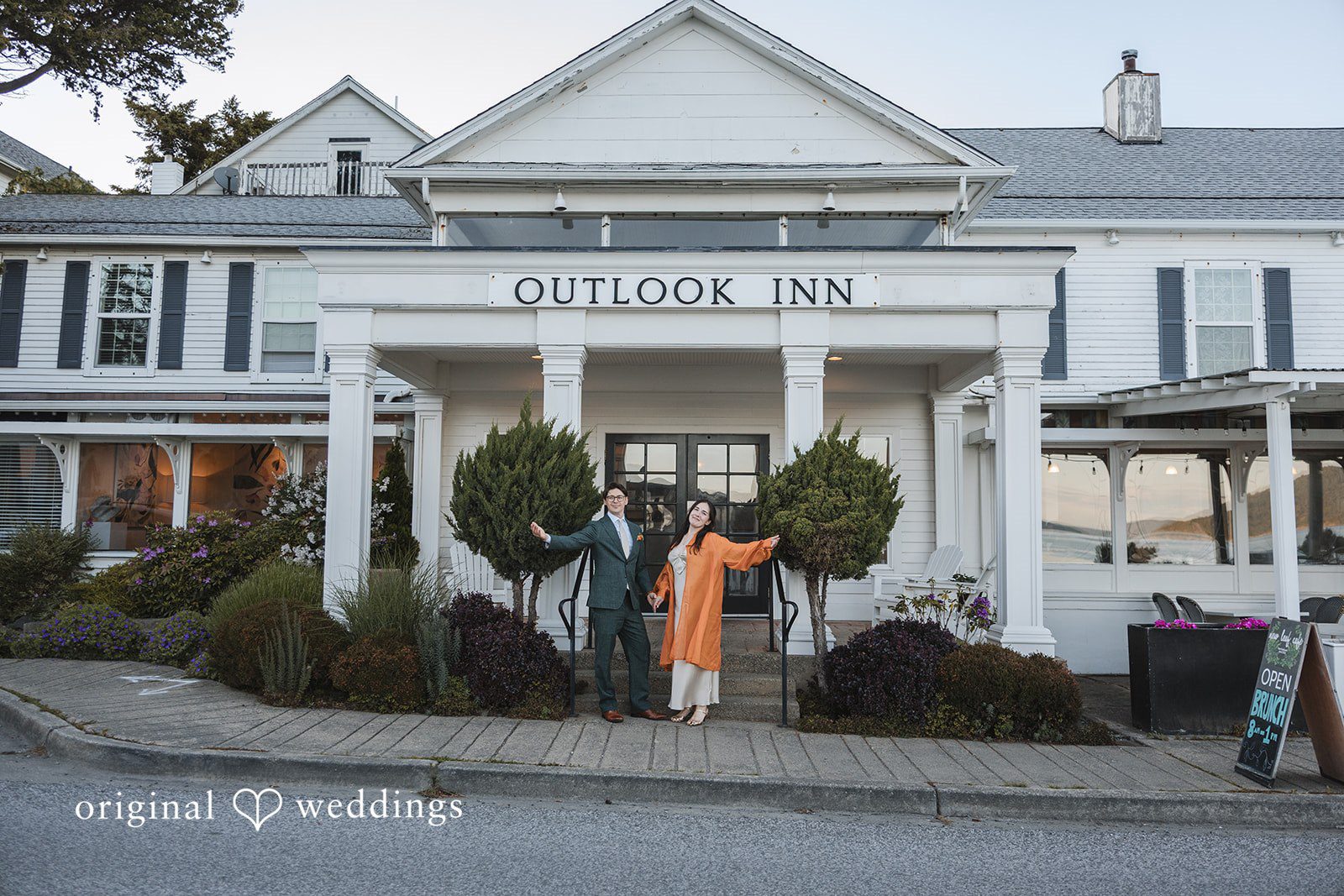 Benjamin + Amber The couple poses joyfully in front of the iconic Outlook Inn entrance after their wedding celebration at Outlook Inn.