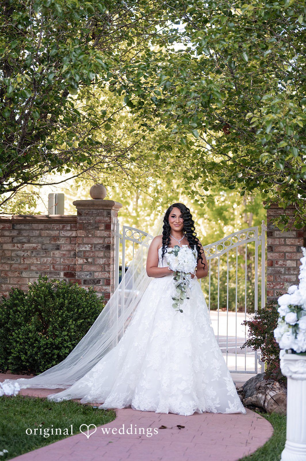 A bride in a large white ballgown standing on a path near a stone wall.