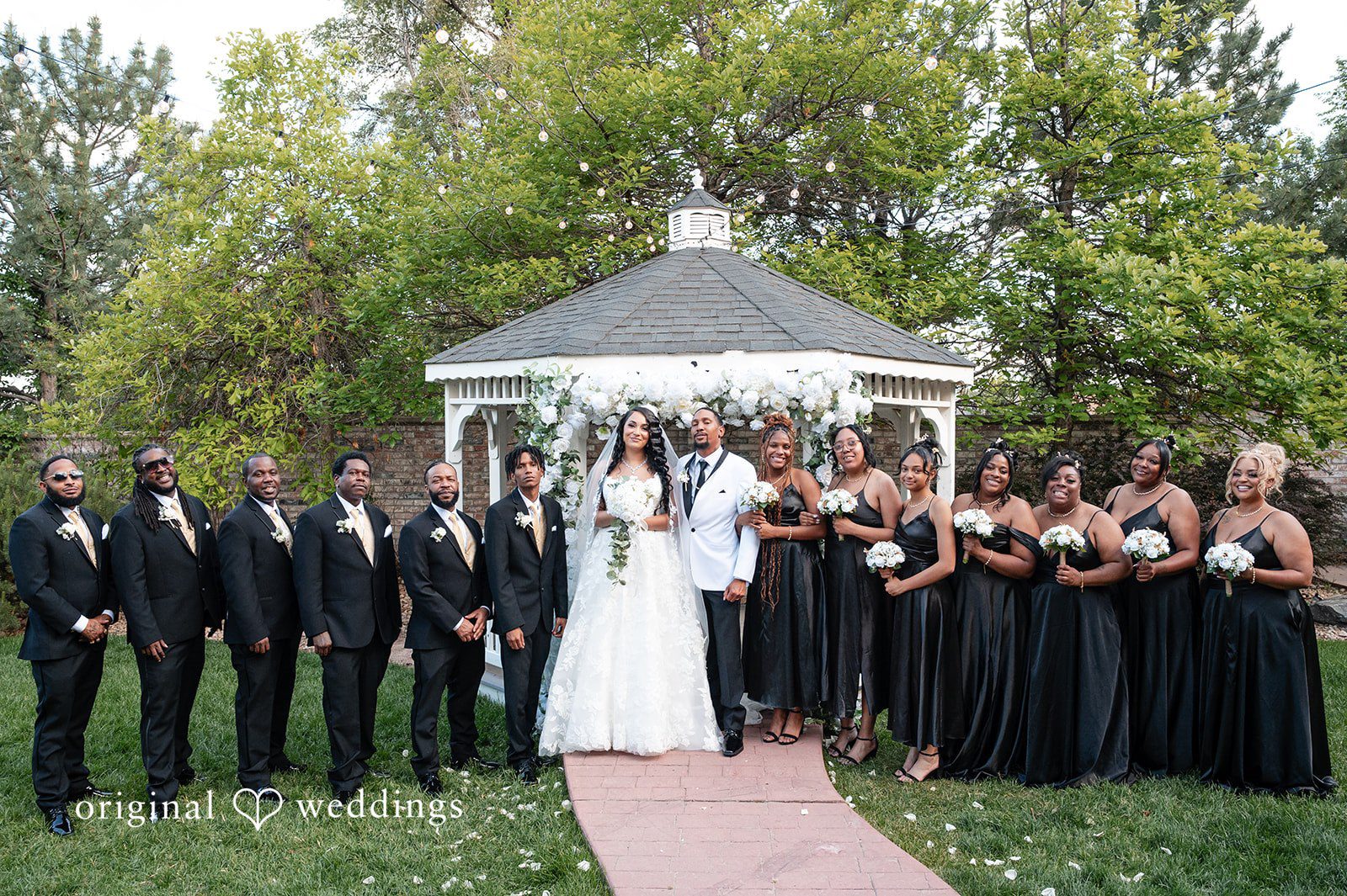 A large wedding party posing together with the bride and groom near a gazebo.