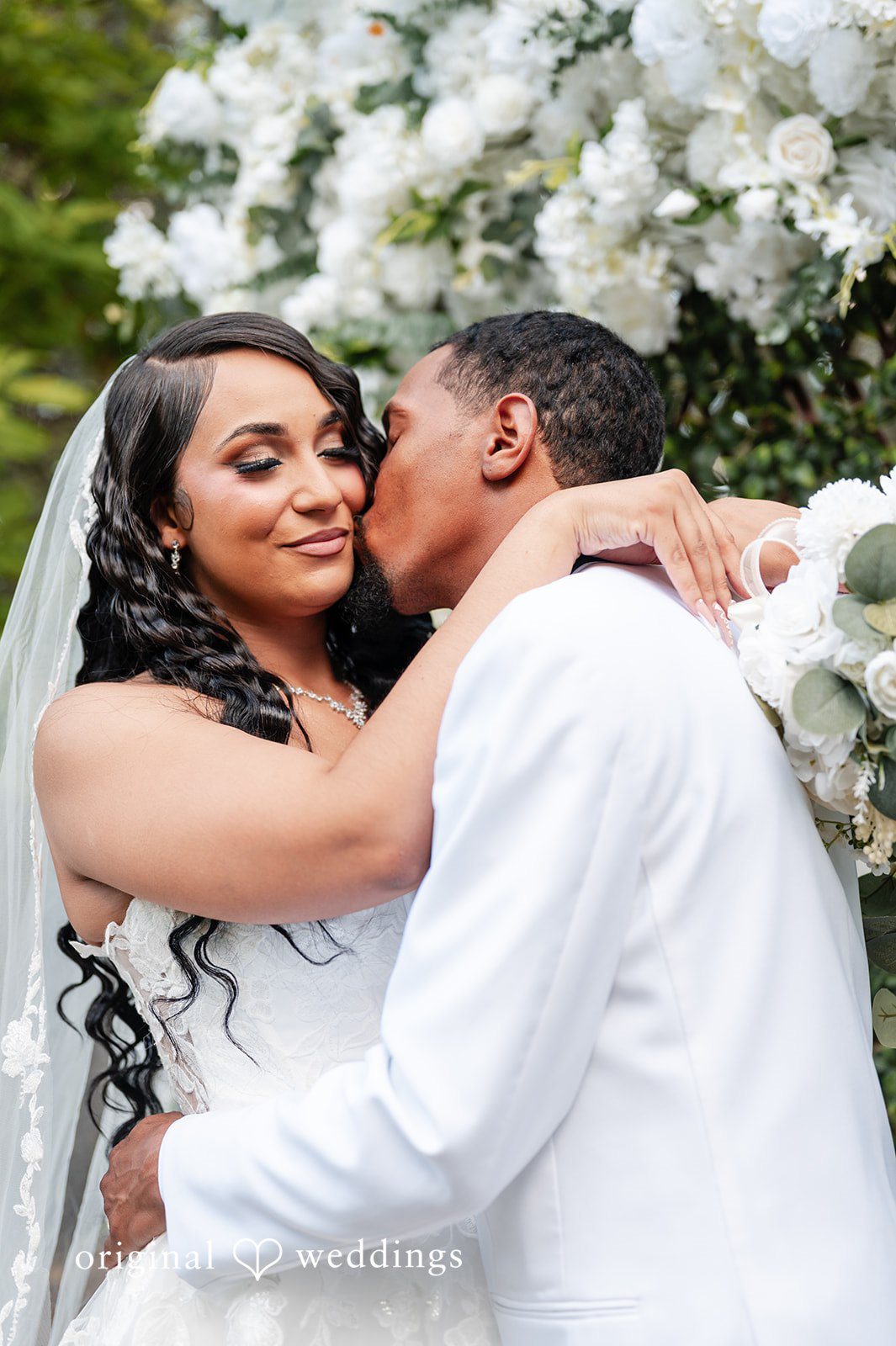 A close-up of a groom kissing a smiling bride on the cheek.