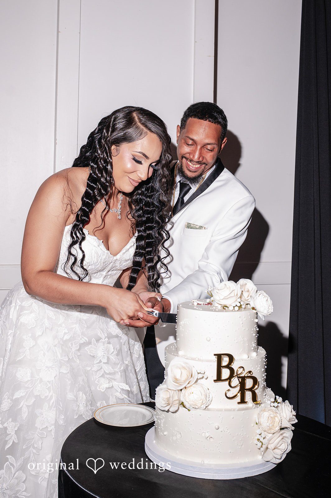 A bride and groom cutting a three-tiered white wedding cake together.
