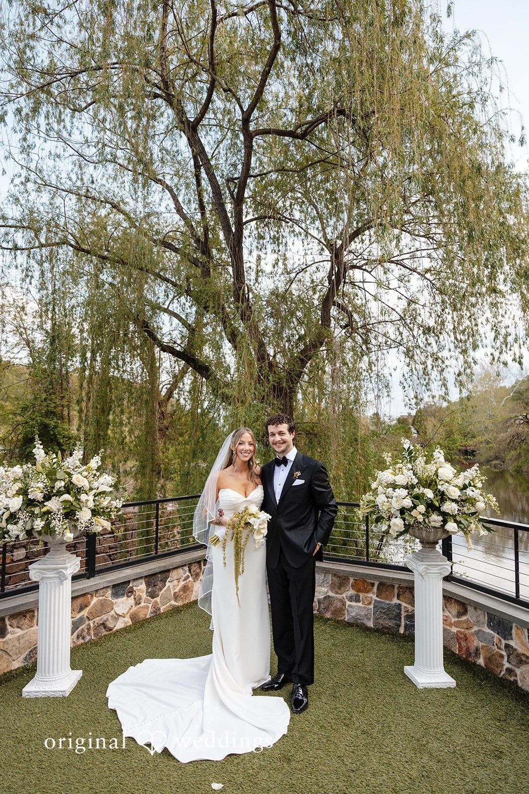 Full-length portrait of the bride and groom beside a tree outdoors