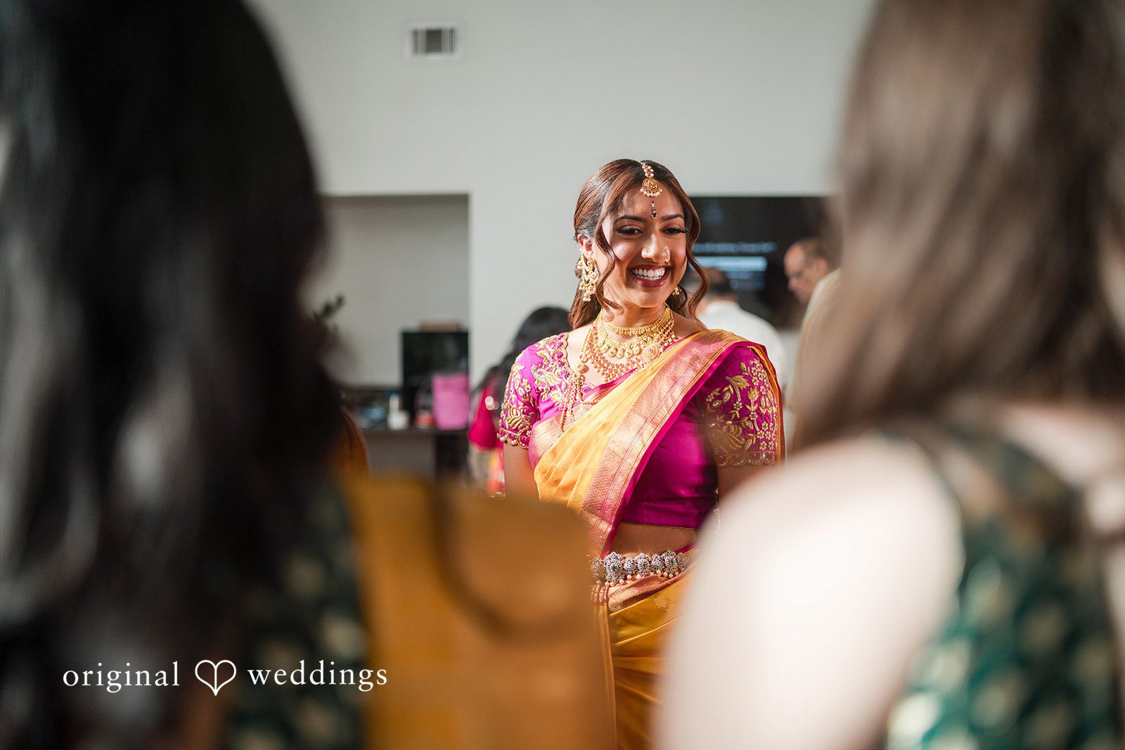 A candid view of a bride wearing a pink saree smiling during a social gathering.