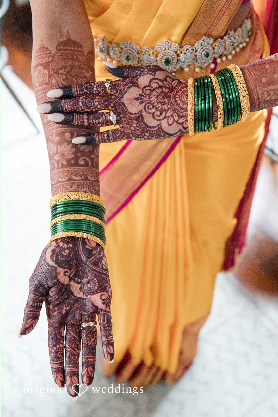A close-up of hands adorned with intricate henna and green bridal bangles.