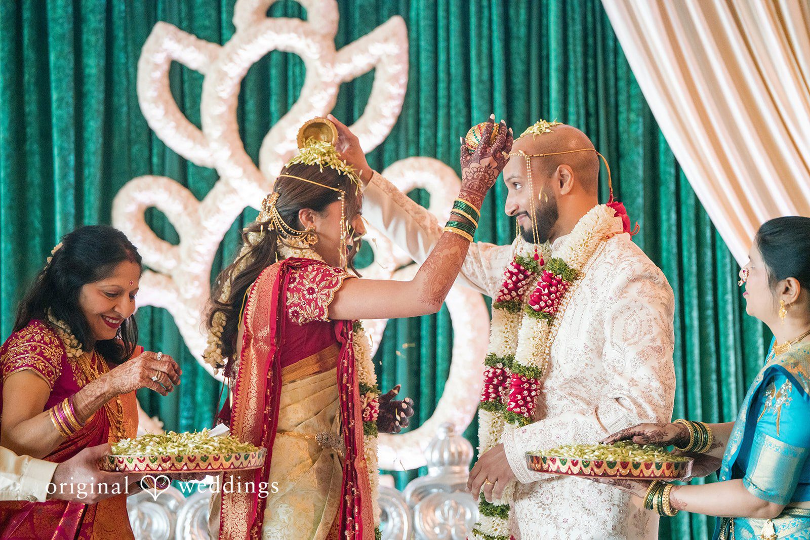 Bride and groom pouring sacred rice over each other's heads during a traditional South Asian wedding ceremony.