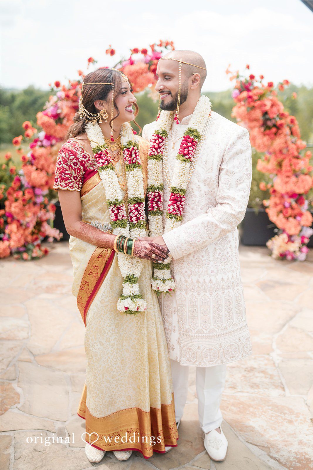 Bride and groom standing together while wearing traditional wedding attire and floral garlands.