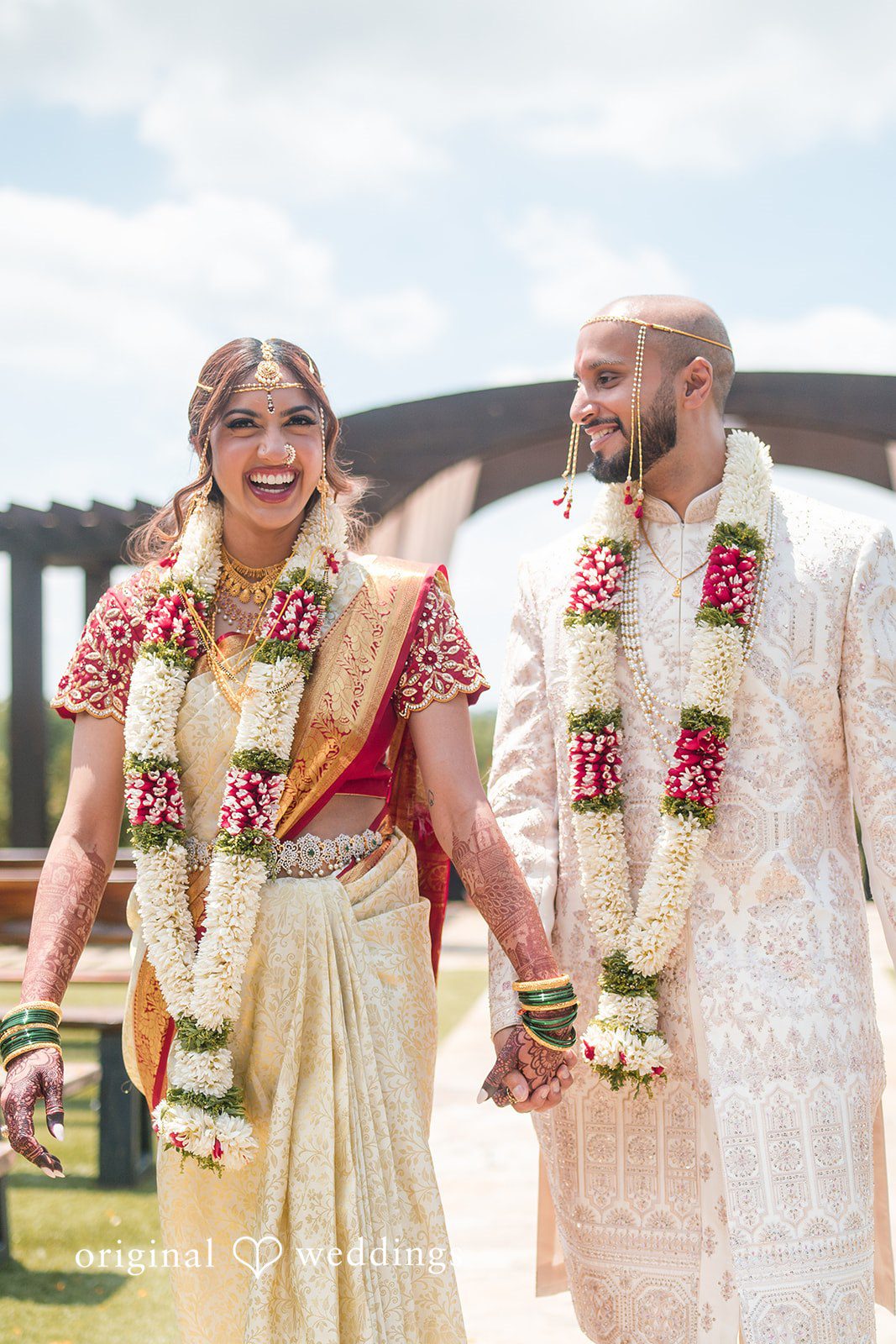 Bride and groom holding hands and smiling while walking together outside.