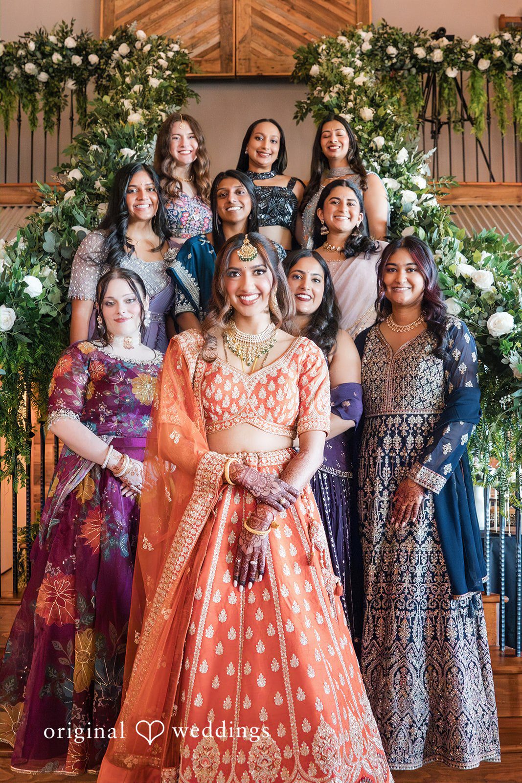Bride posing on a decorated staircase with female wedding guests standing behind her.