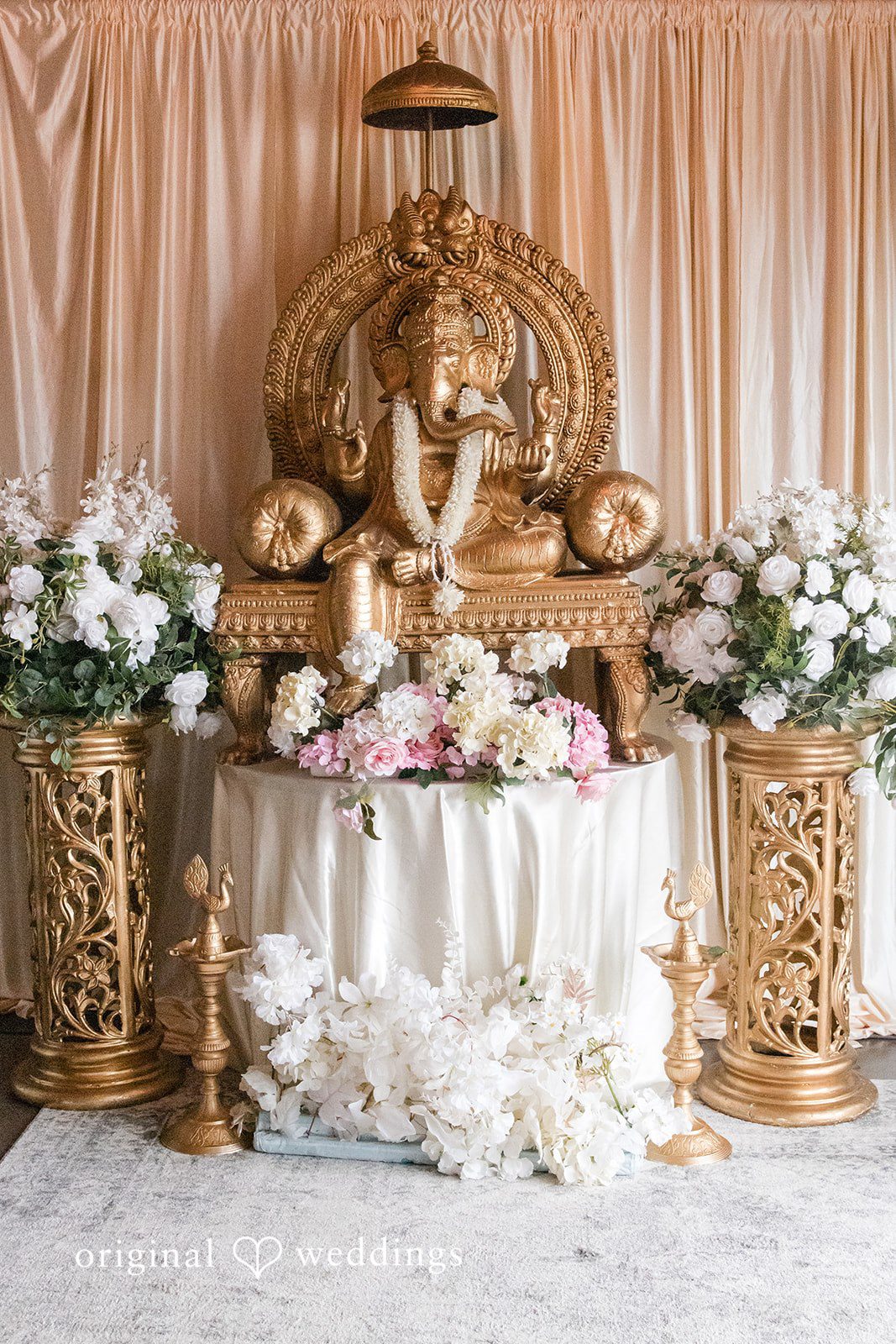 A decorated altar featuring a golden statue of Ganesha flanked by floral arrangements on elegant stands.