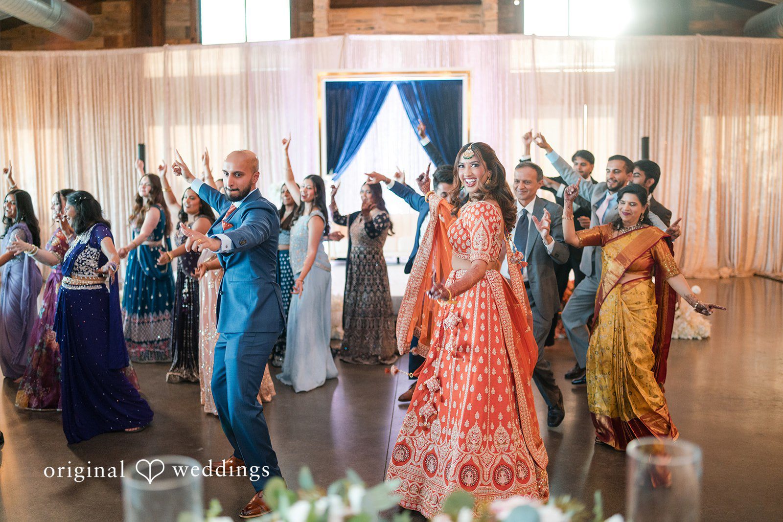 Large group of wedding guests dancing together during a reception celebration.