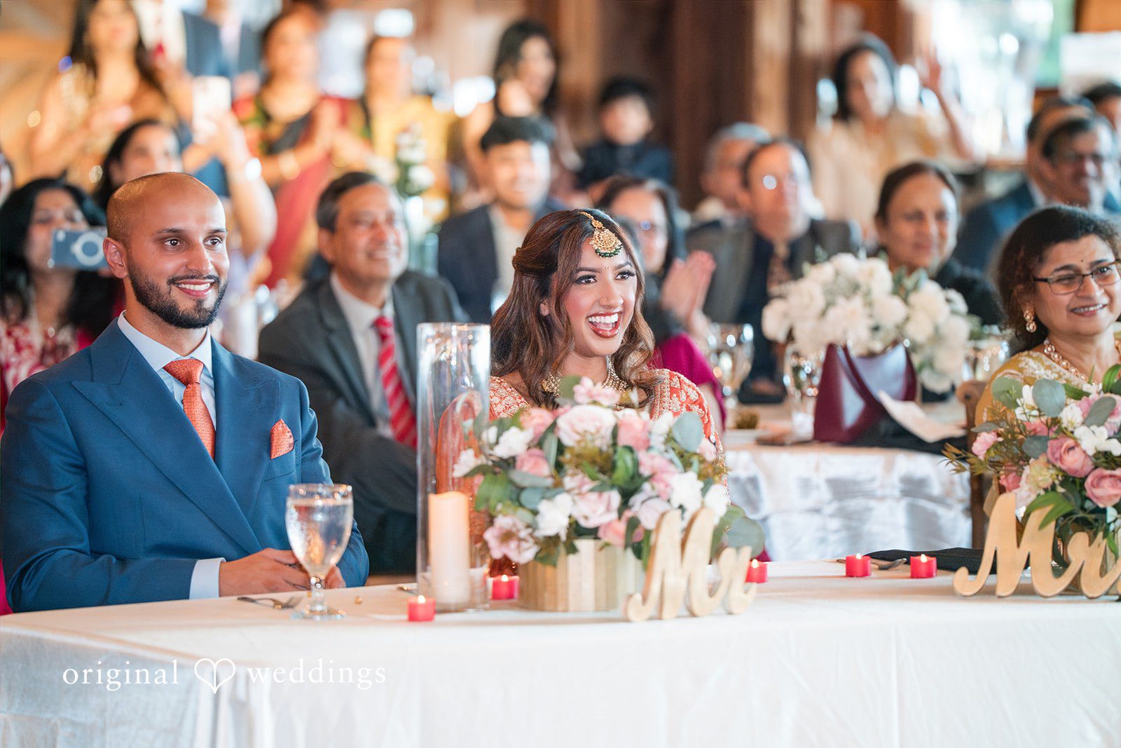 Wedding guests in formal and traditional clothing seated together at a reception table.