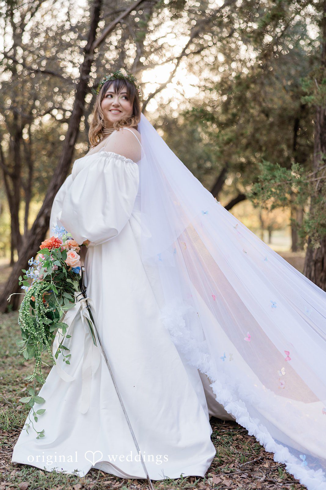 Brittney + Benjamin A bride in a white gown and long veil posing among trees.