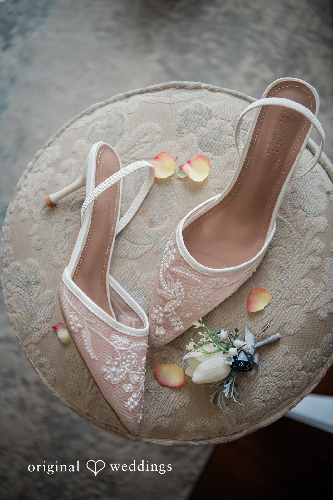Brittney + Benjamin High-heeled bridal shoes and wedding bands placed on a decorative surface.
