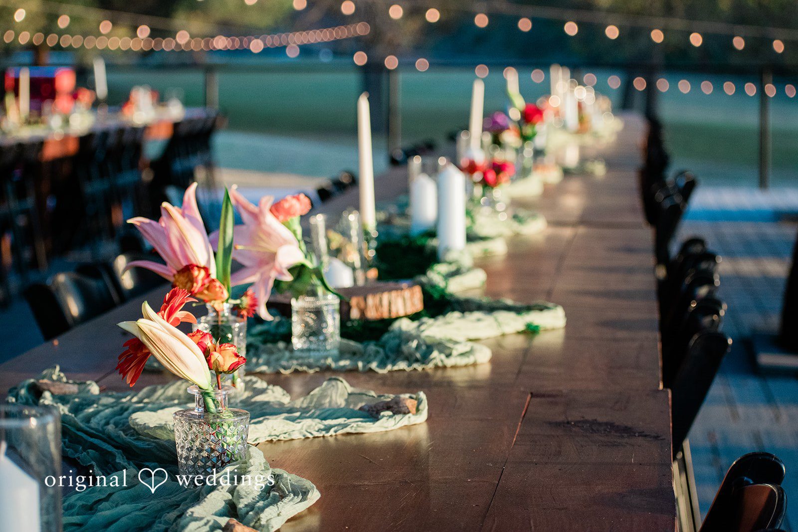 Brittney + Benjamin A long dinner table decorated with colorful floral arrangements, candles, and glassware.