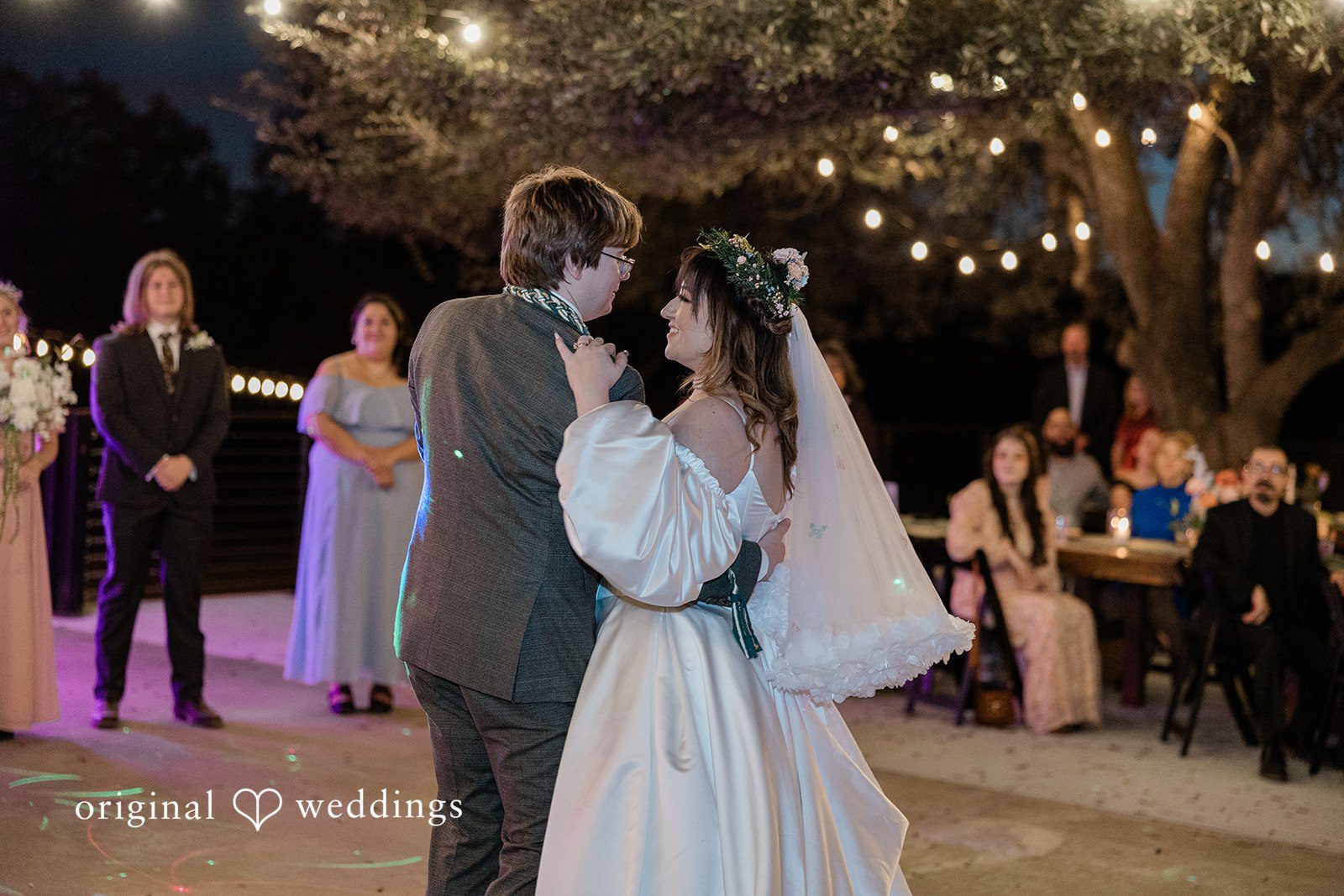 Brittney + Benjamin A bride and groom dancing together at their reception with guests in the background.