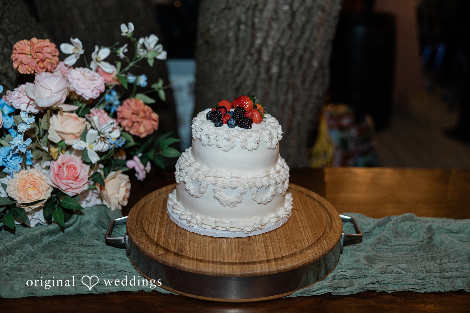 Brittney + Benjamin A tiered white wedding cake topped with red fruit on a wooden stand.