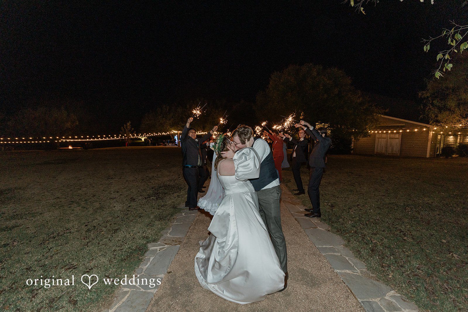 Brittney + Benjamin A bride and groom walking down a path at night surrounded by sparklers.