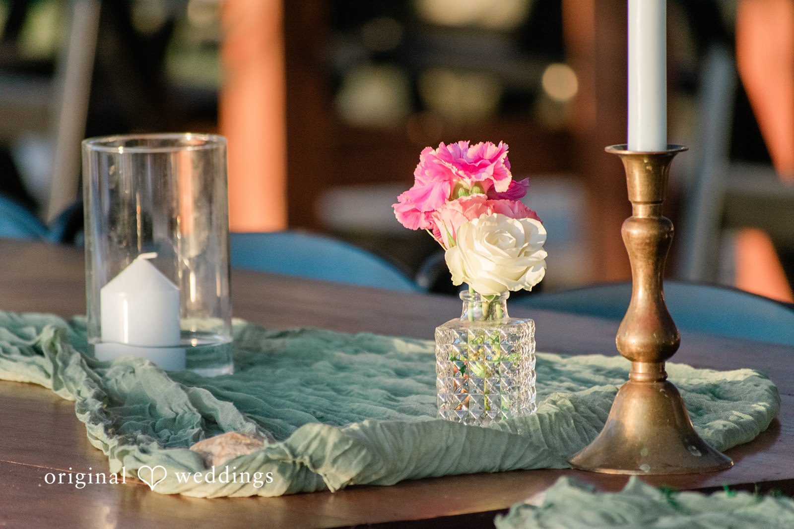 Brittney + Benjamin Table centerpiece featuring a pink flower in a vase, candles, and a green runner.