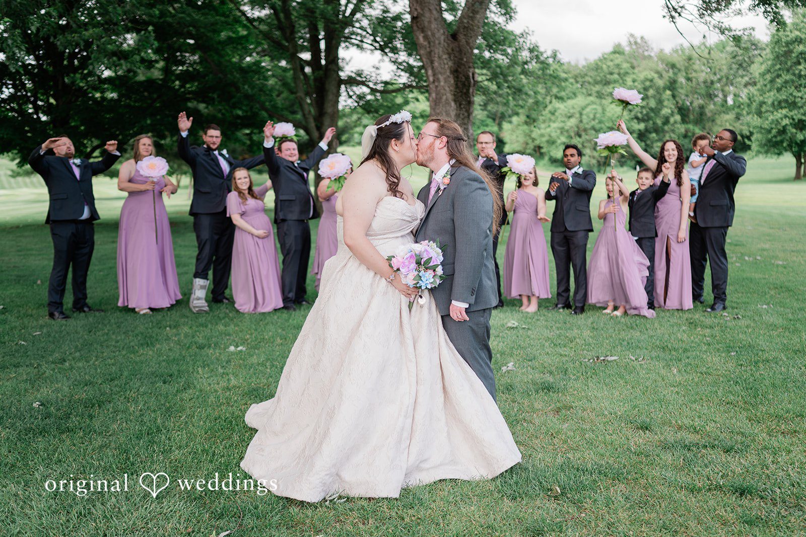 Couple sharing a kiss while bridesmaids and groomsmen cheering behind