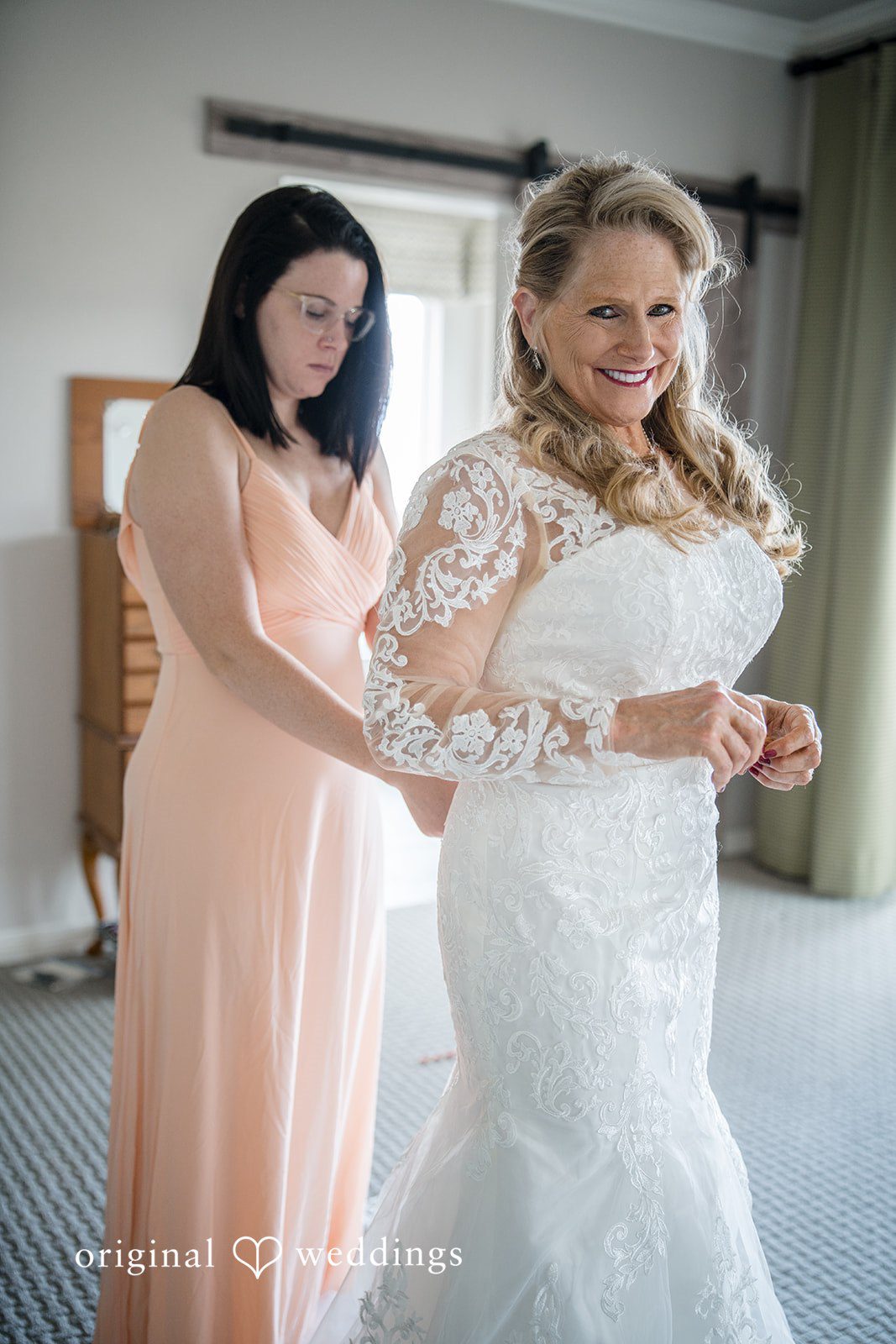 Jacquelyn + Millard Bride smiling while getting help with her wedding dress during bridal preparations.