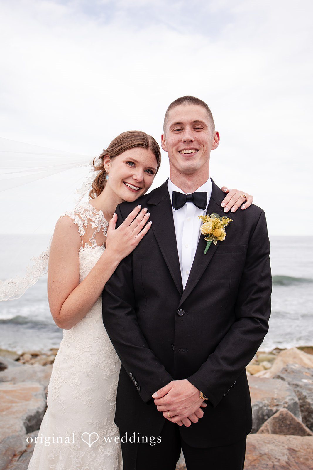 Alanna + Stan Bride smiles while resting her hand on groom’s shoulder during seaside wedding portrait.