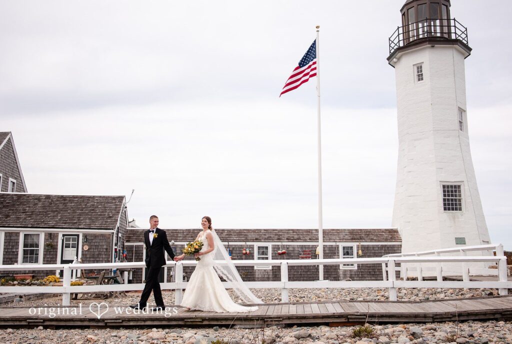 Alanna + Stan Bride and groom walk hand in hand near lighthouse at The Barker House captured by Boston wedding photographers from Original Weddings