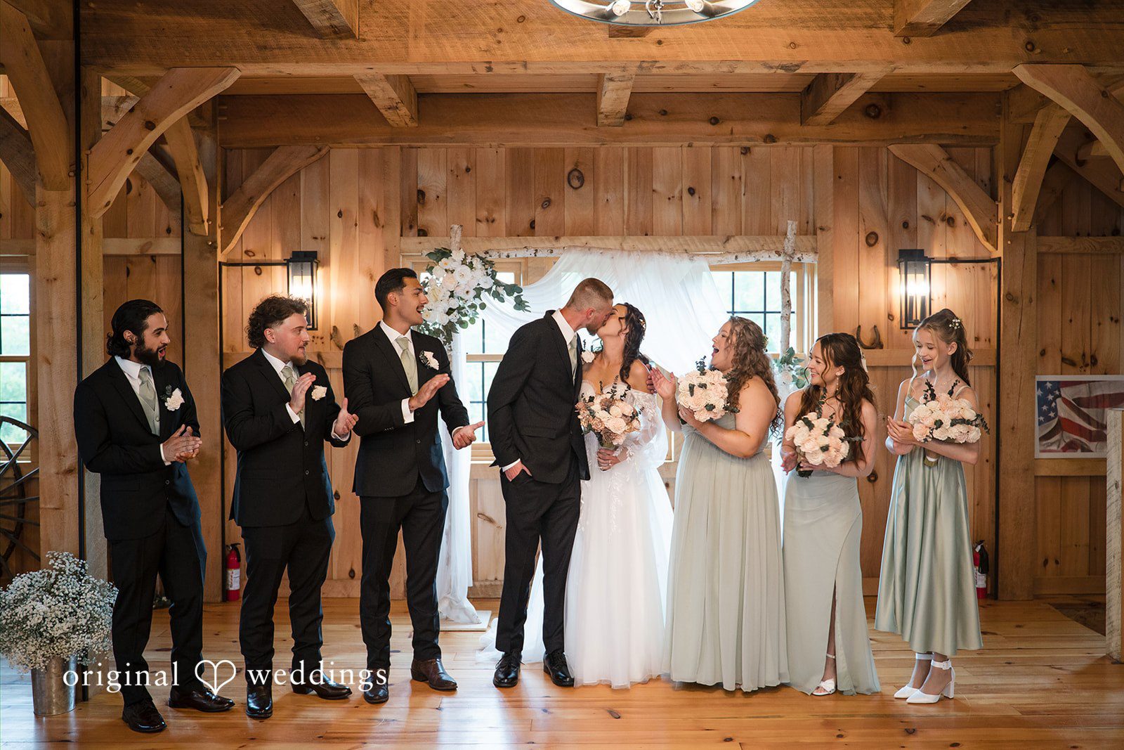 Nicole + Dalton Bride and groom sharing a kiss while groomsmen and bridesmaids are all around cheering