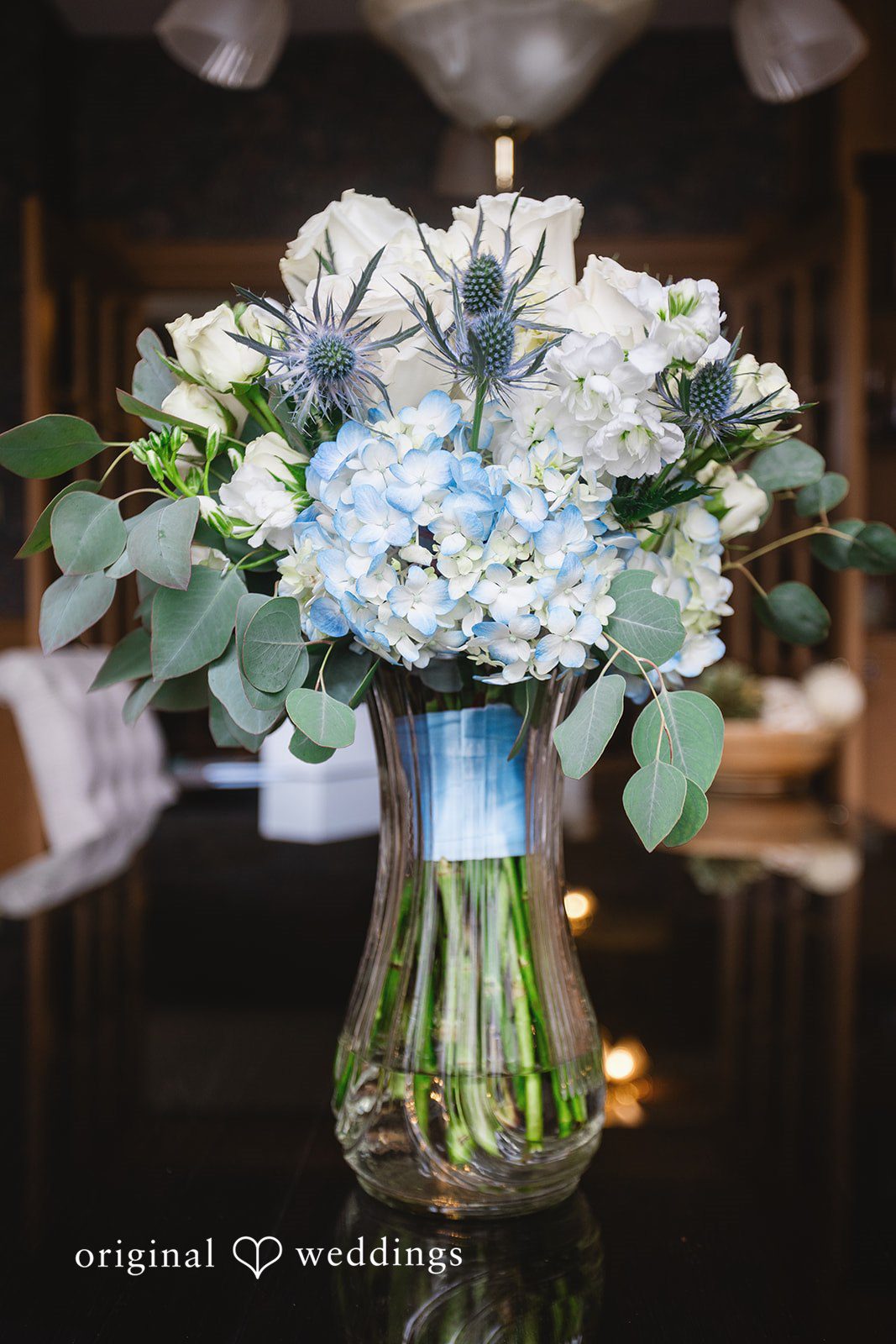 A wedding floral centerpiece featuring white and light blue flowers arranged in a glass vase.