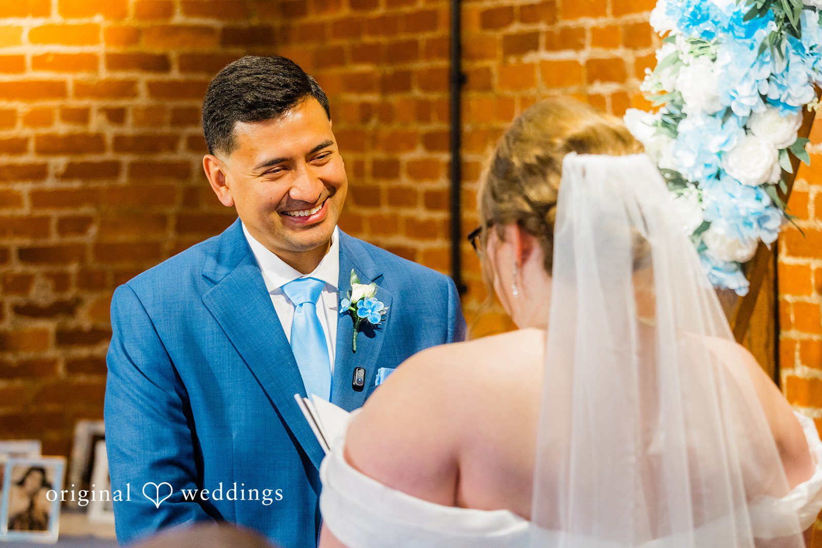 A smiling groom in a blue suit looking at his bride during the wedding ceremony.