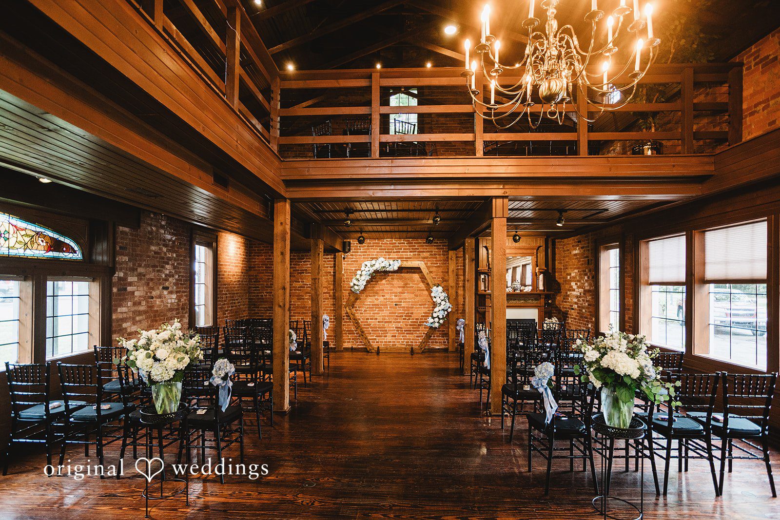 A wedding reception venue featuring long wooden tables, dark chairs, and floral centerpieces.