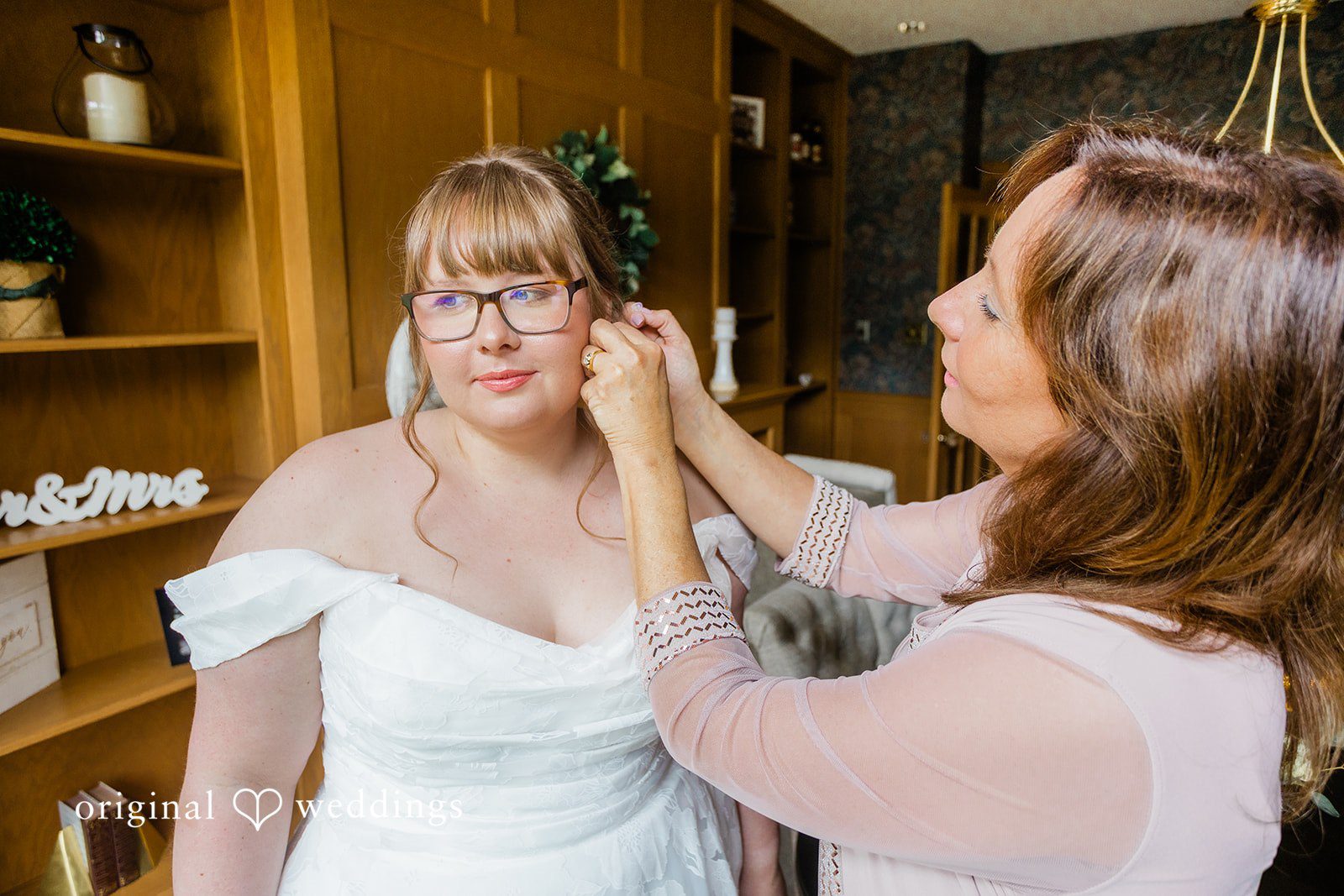 A bride wearing a white off-the-shoulder wedding gown while having her hair styled.