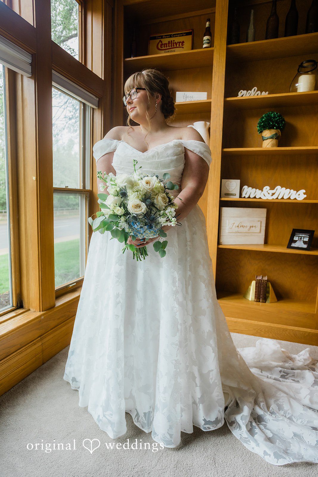 A smiling bride wearing a white off-the-shoulder wedding gown and holding a bouquet.