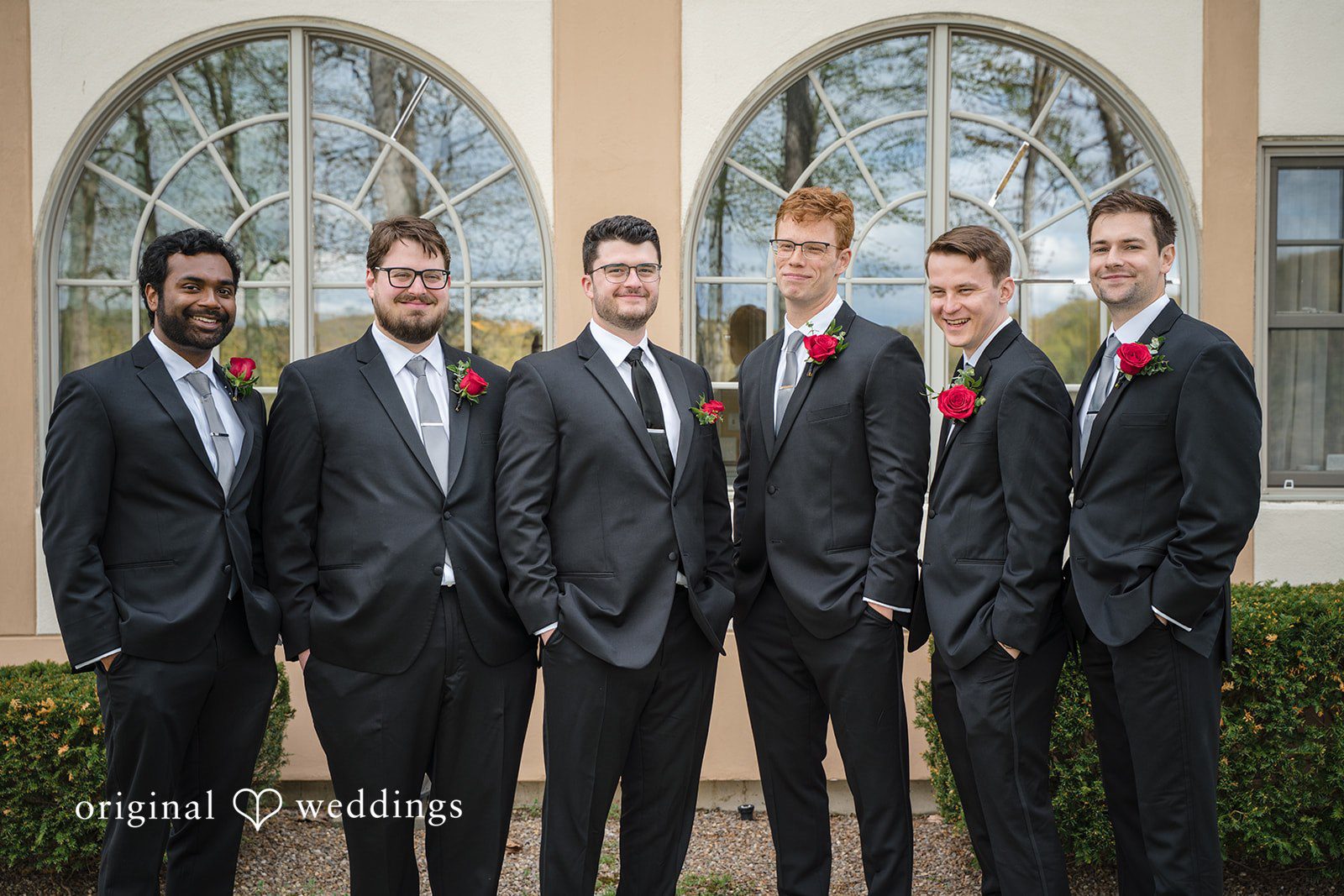 Stylish groom squad in black suits with red rose boutonnieres