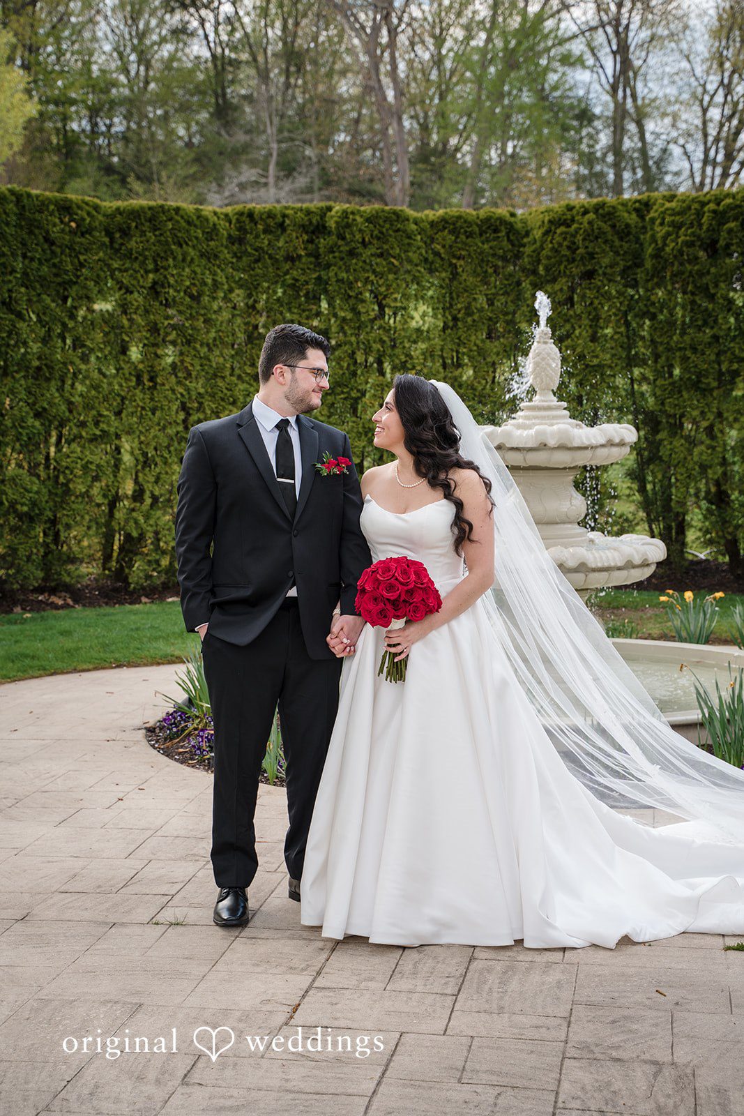 Newlywed couple holding hands beside garden fountain