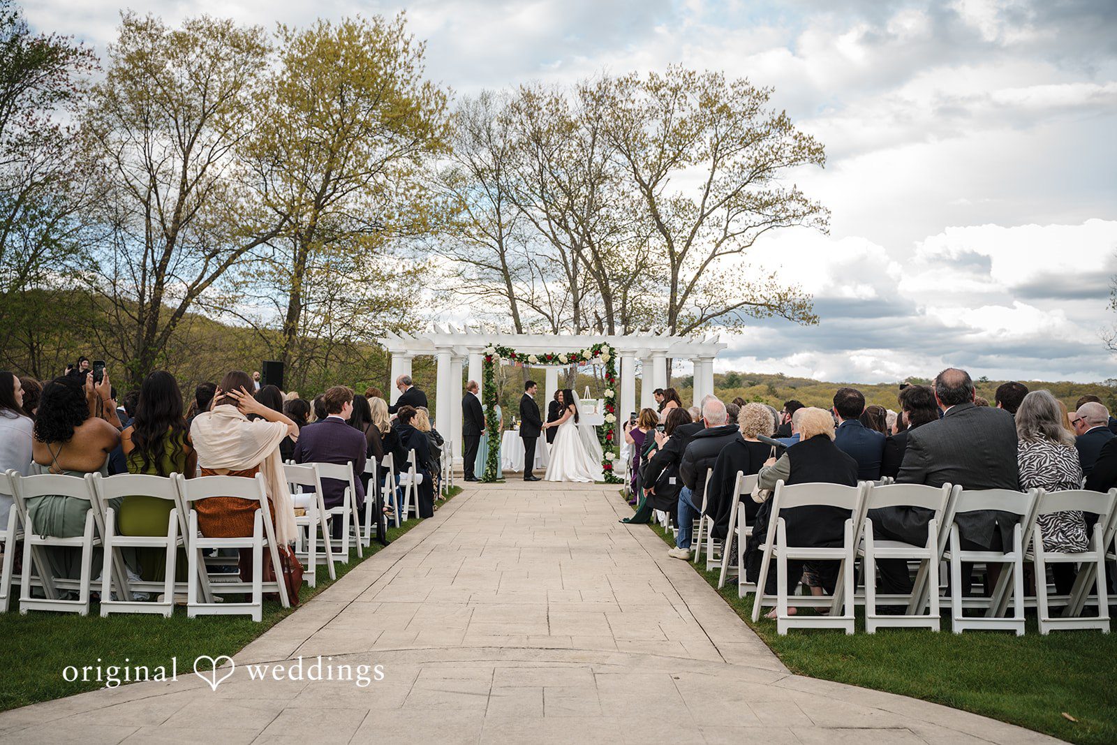 Elegant outdoor ceremony setup with white chairs and floral wedding arch.